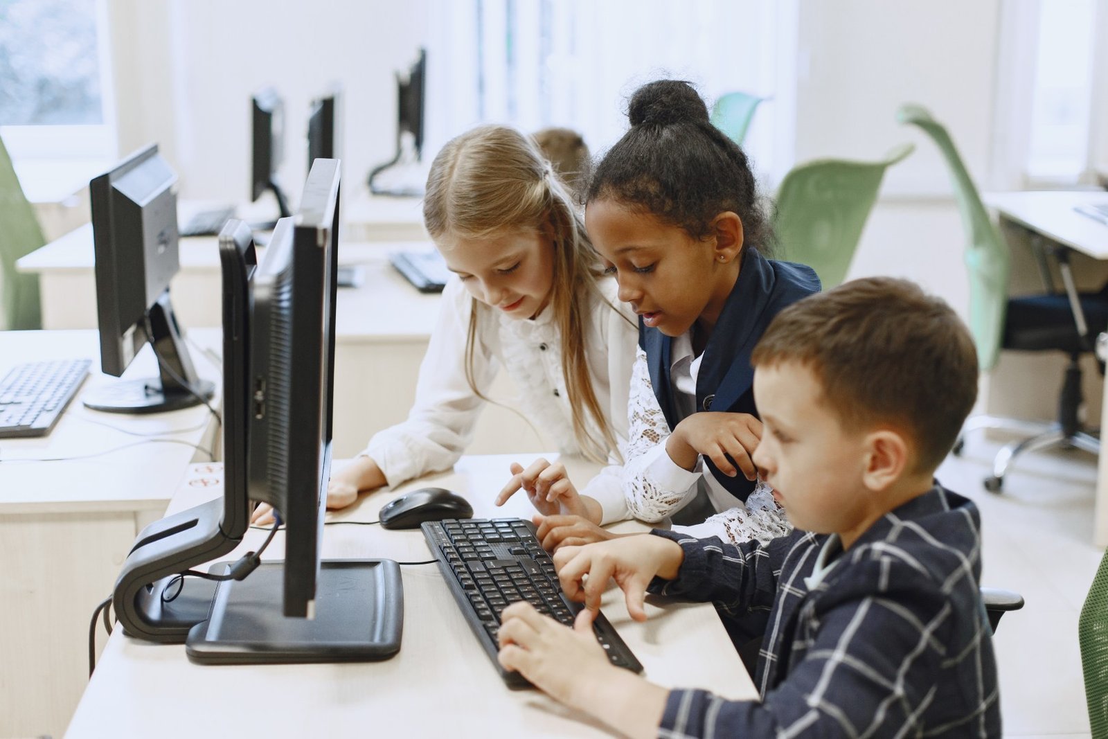 Three young children sharing a desktop computer at a classroom desk